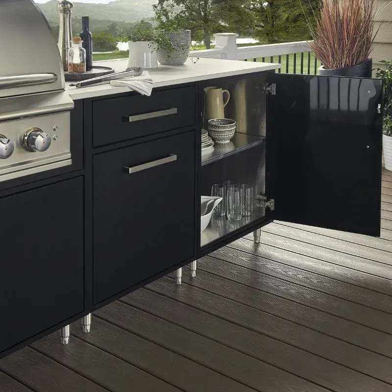 Outdoor kitchen with black cabinets, stainless steel grill, and white countertop. A cabinet door is open, revealing shelves.