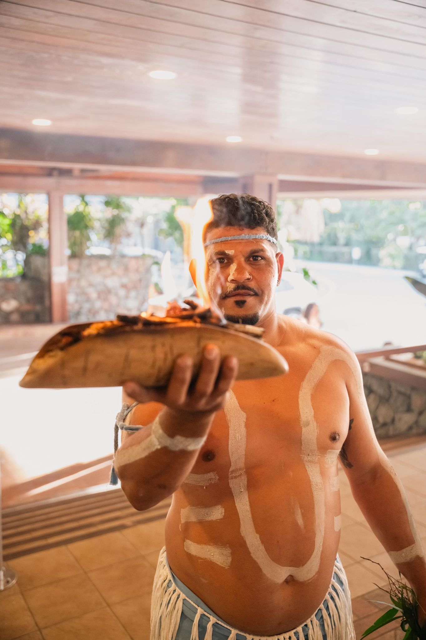 A shirtless man is holding a piece of wood with flames coming out of it.