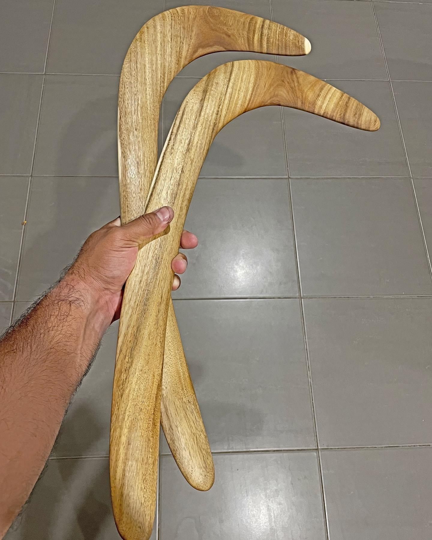 A person is holding two wooden boomerangs in their hand.