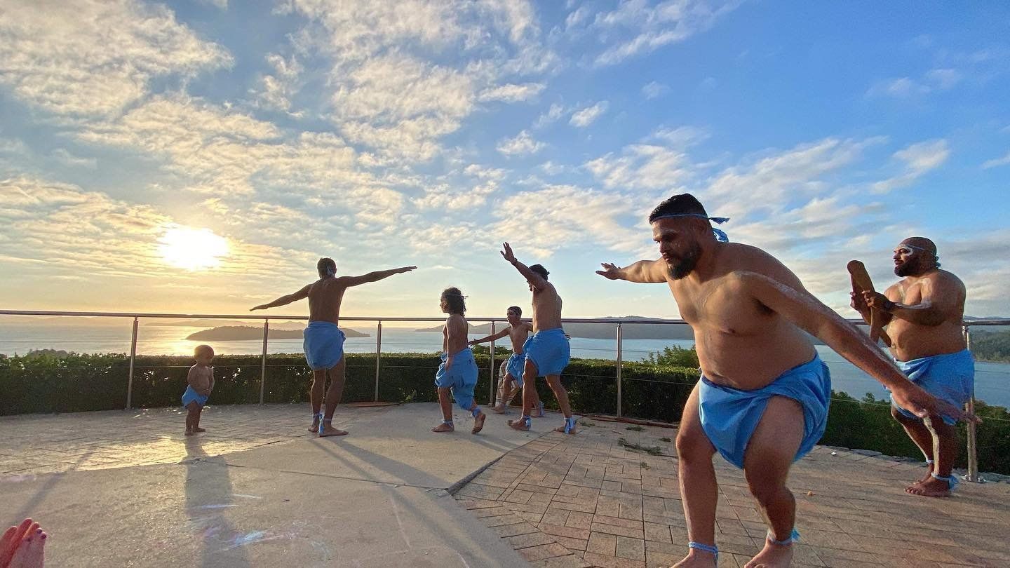 A group of men are dancing on a beach at sunset.