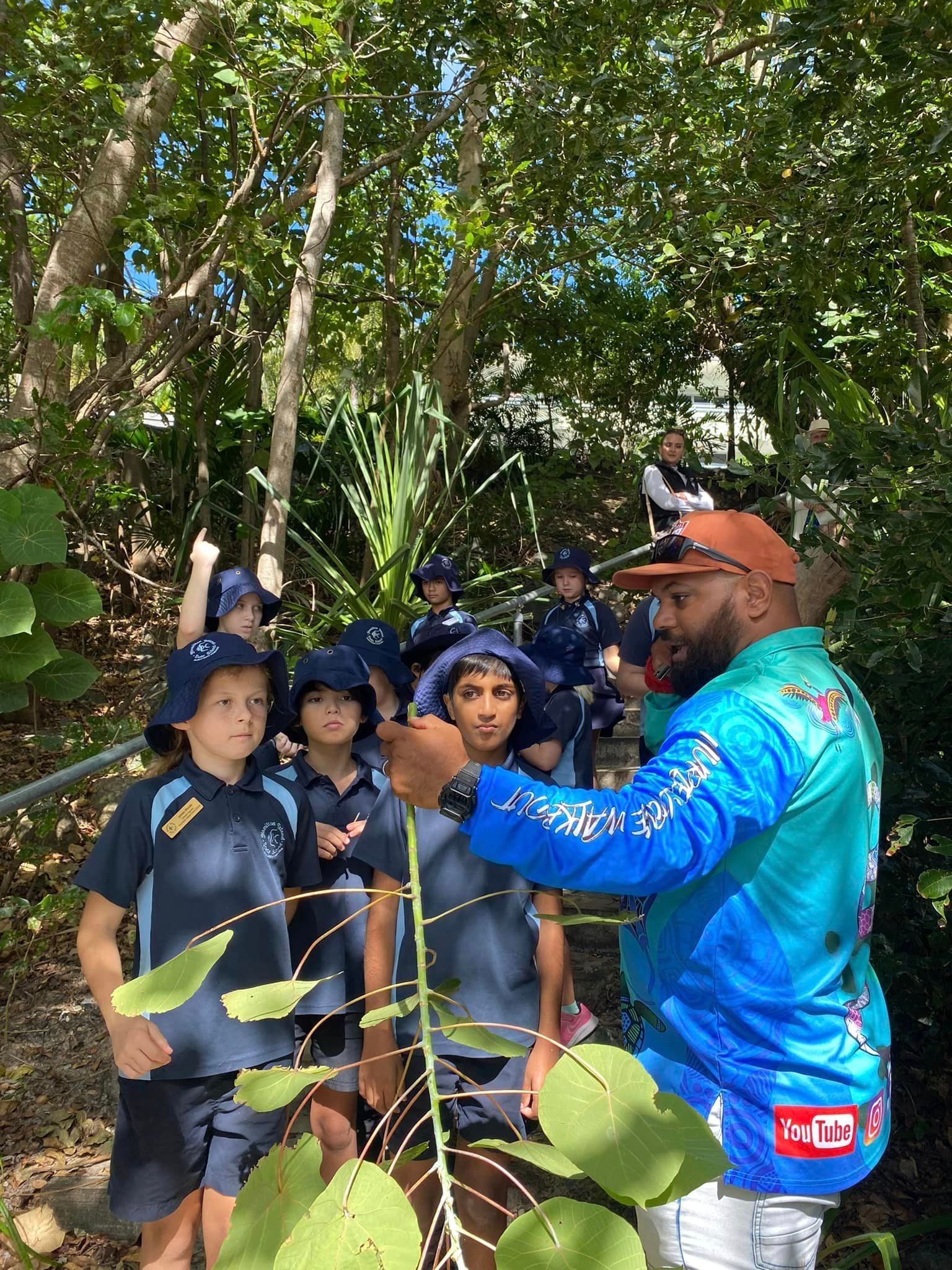 A man is teaching a group of children about plants in the woods.