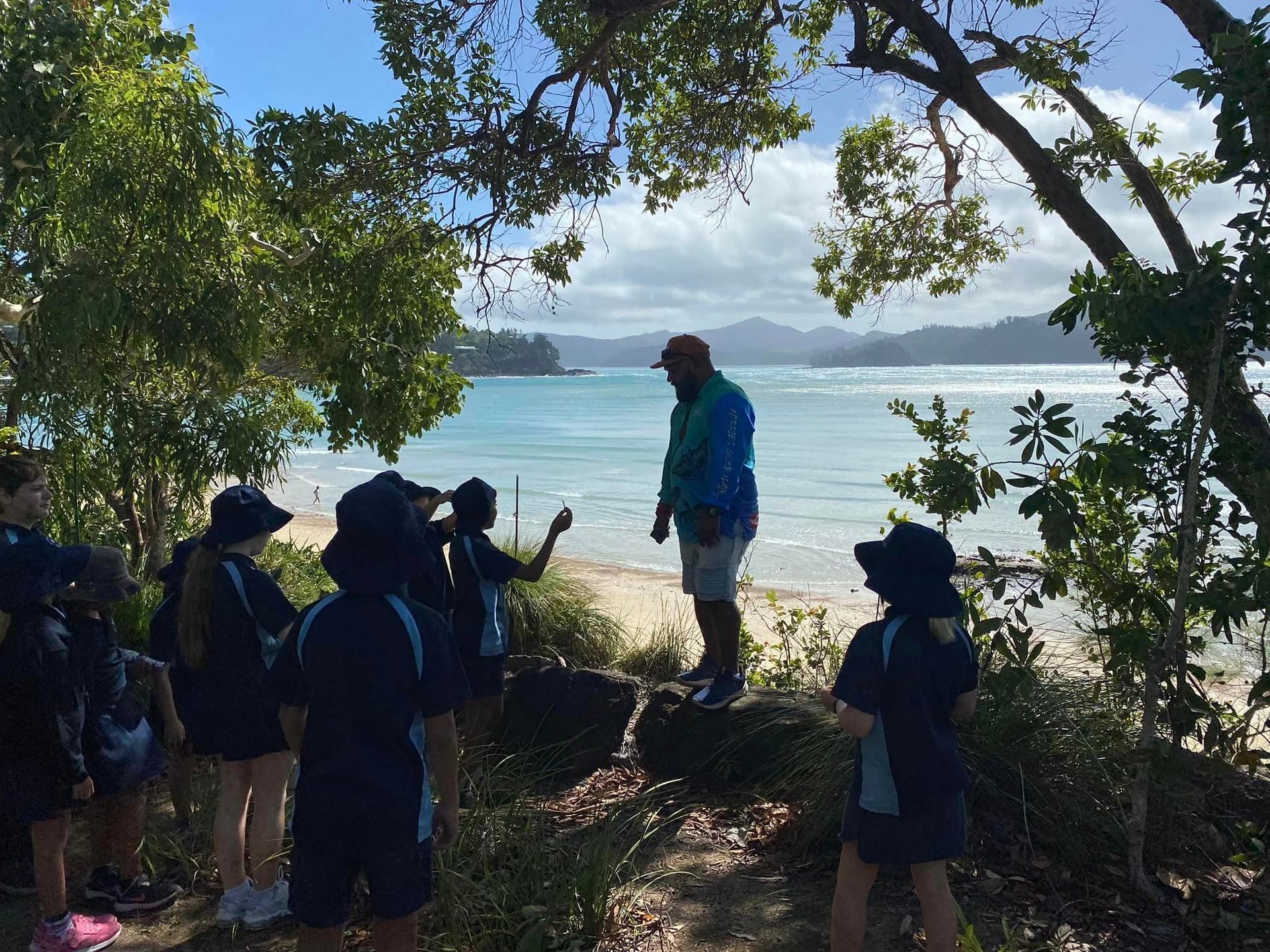 A group of people are standing on a rock near a beach.