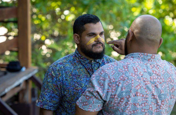 Two men are standing next to each other and one of them is applying a bandage to the other 's nose.