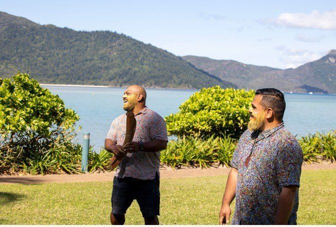 Two men are standing next to each other in front of a body of water.