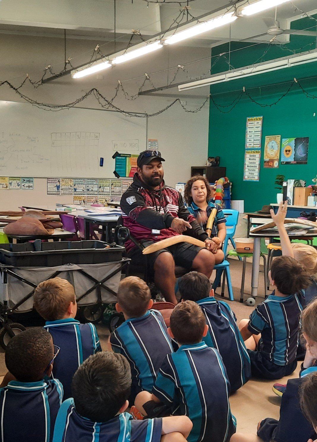A man is sitting in front of a group of children in a classroom.