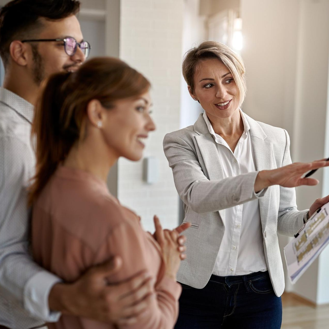 Three people discuss a large presentation board in a bright office, one pointing and smiling.