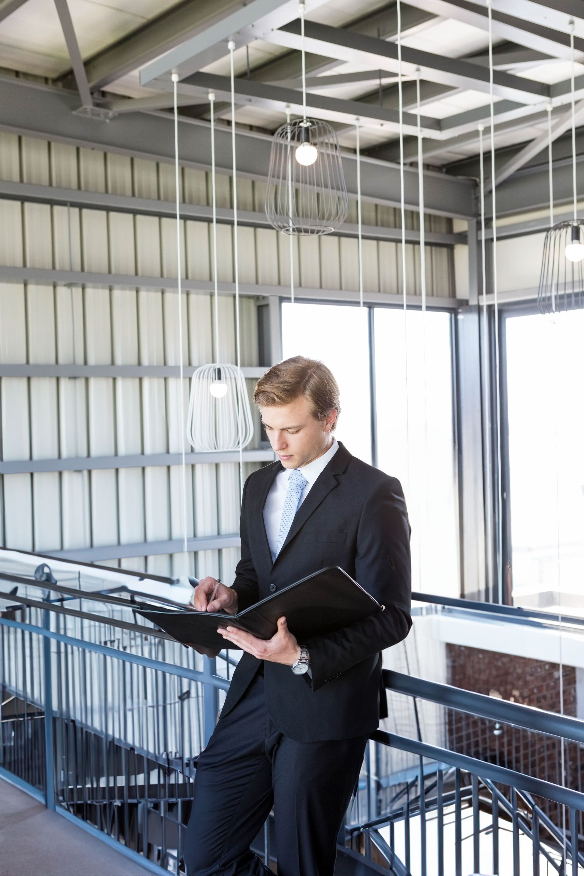 Man in a suit writing on a clipboard in an industrial-style balcony corridor
