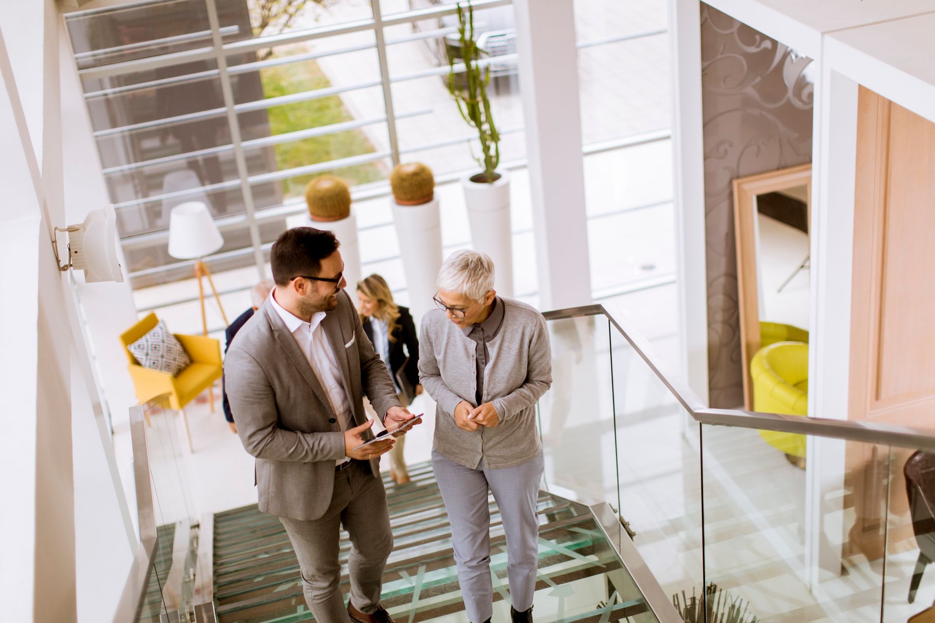 Three professionals walking up stairs in a bright office lobby, discussing a device.