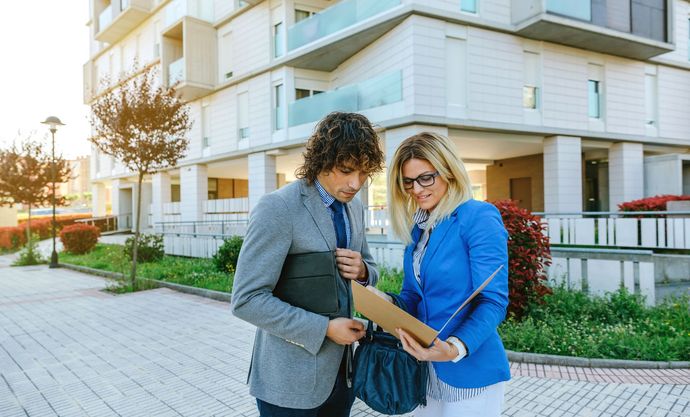 Two people reviewing a document outside a modern apartment building at sunset