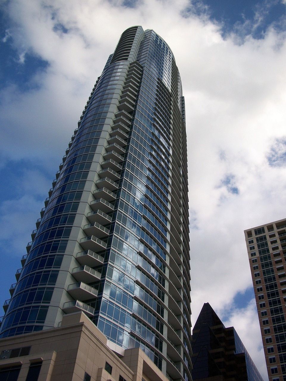 Tall glass skyscraper against a cloudy sky, with nearby buildings at the edges