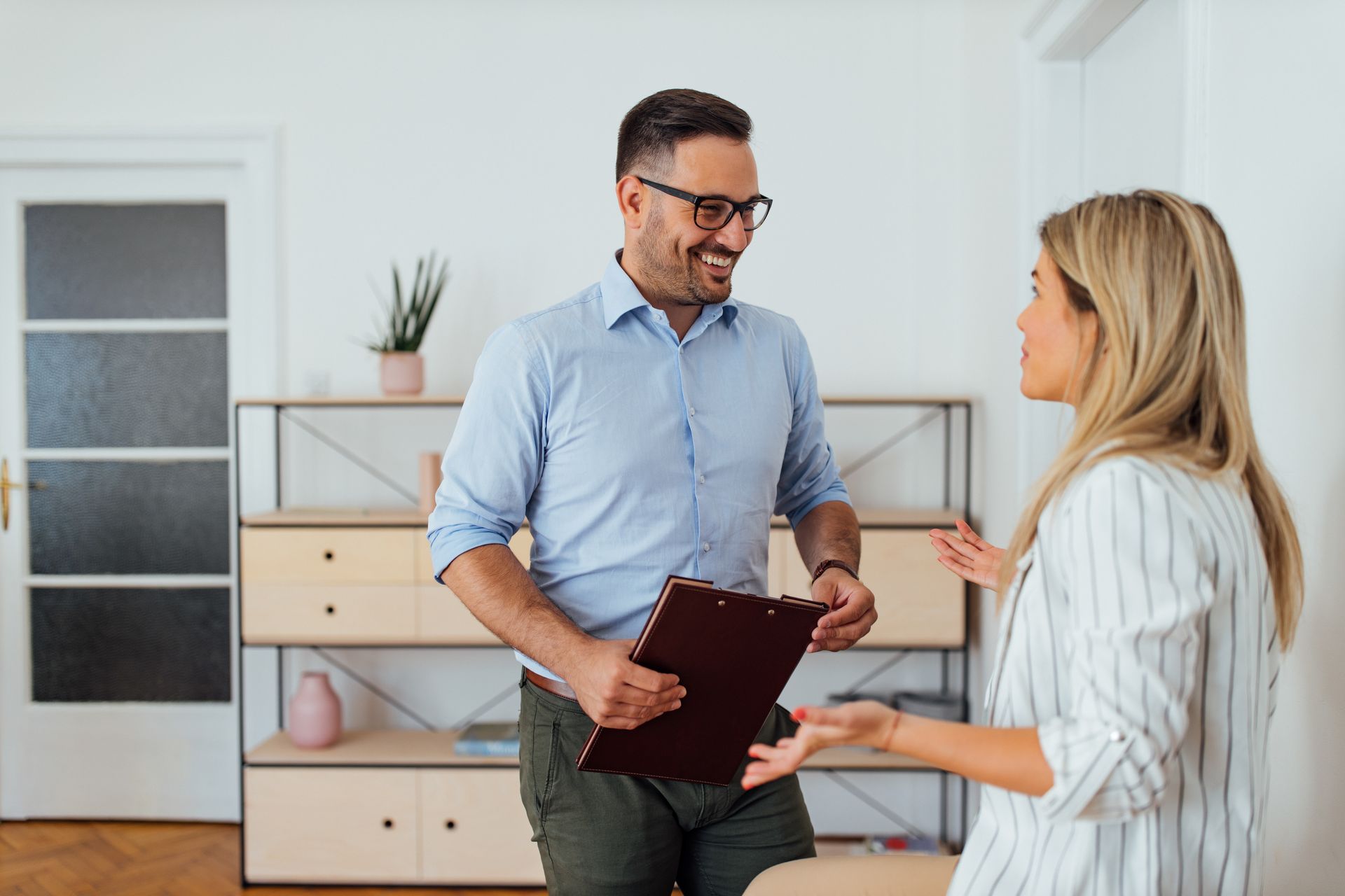 Two people talking in a bright office, one holding a red folder and smiling.