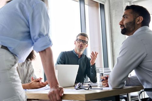 Business meeting with three people around a table, discussing a laptop in a bright office.