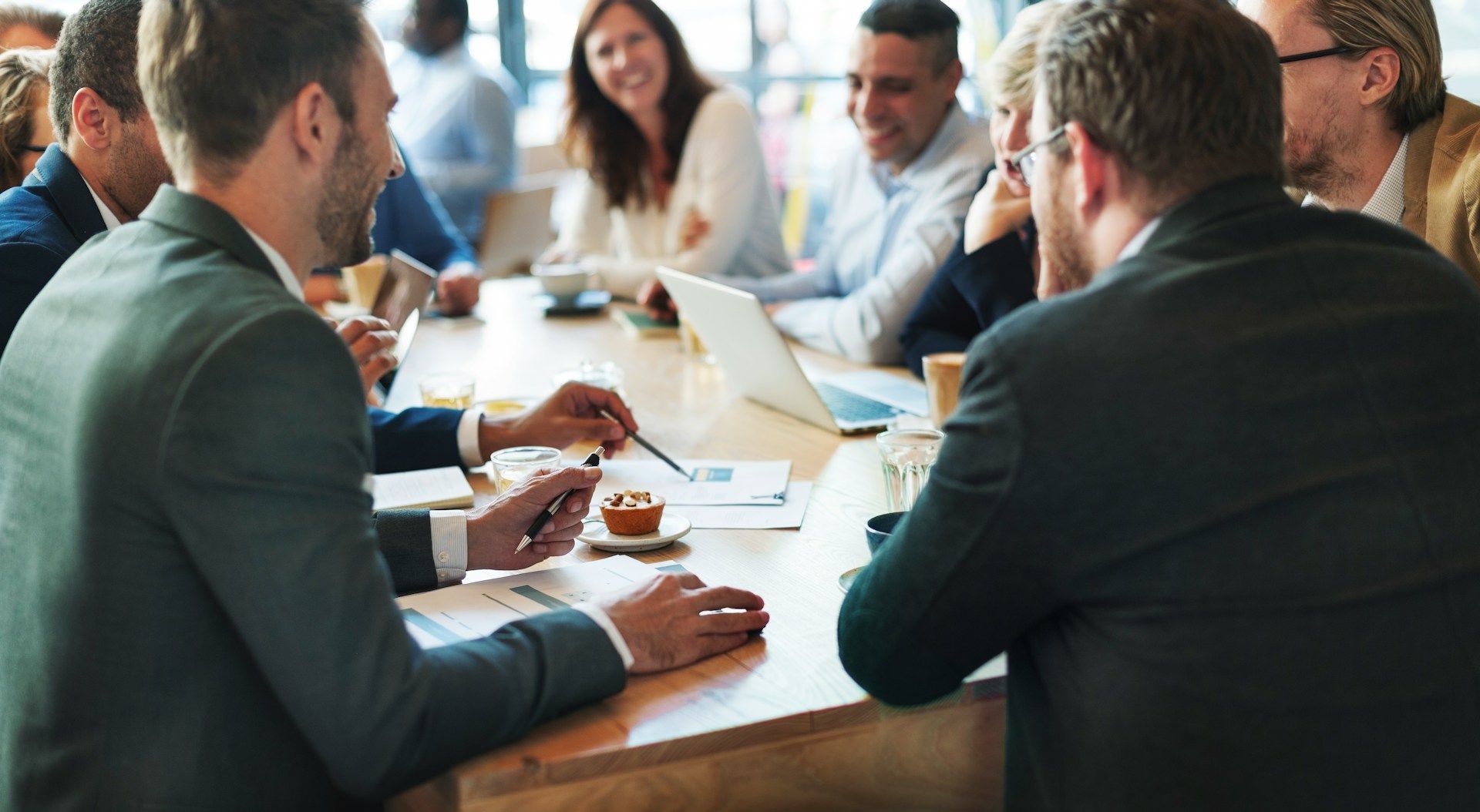 Colleagues seated around a conference table in a meeting room, discussing over coffee and notes