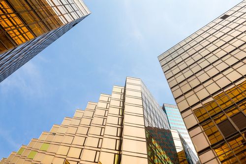 Looking up at modern glass-and-steel skyscrapers against a bright blue sky