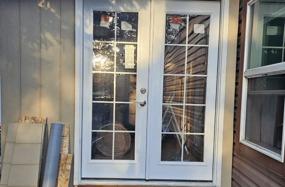 White double doors with glass panes, between siding and a window.