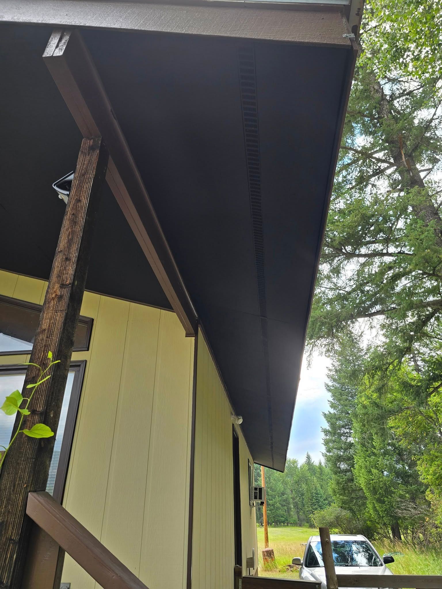 Black eaves of a house with a brown support beam. Yellow siding. Tree and sky visible.