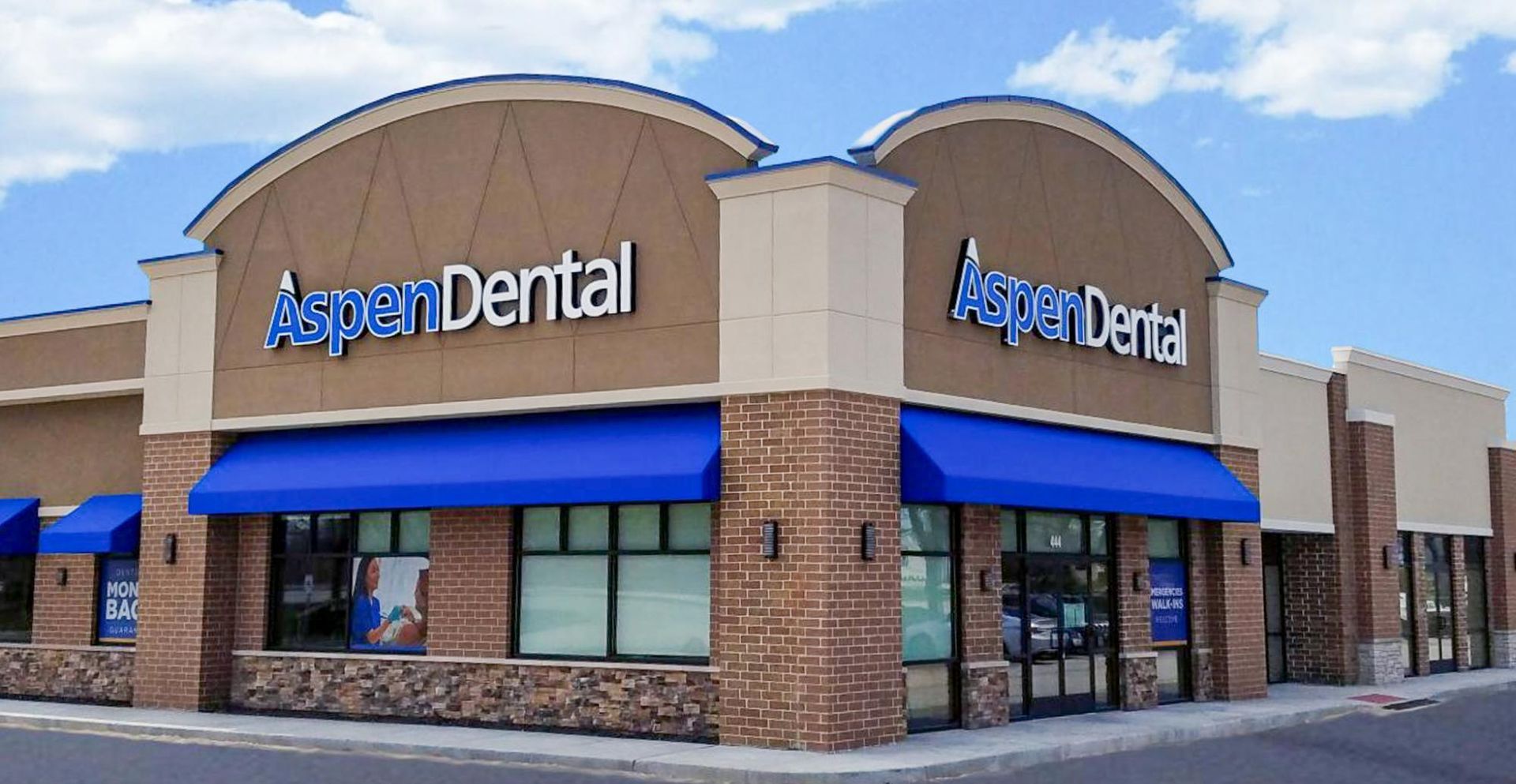 Aspen Dental storefront with tan brick exterior and blue awnings at a shopping plaza