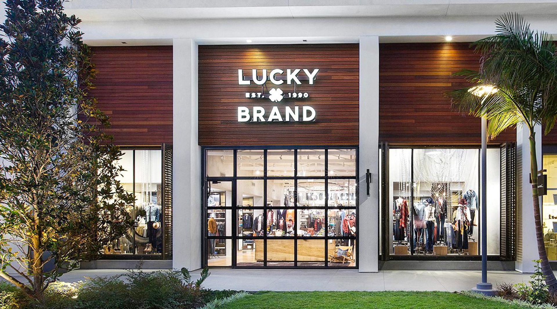 Lucky Brand clothing store storefront with large windows and warm wood paneling at dusk
