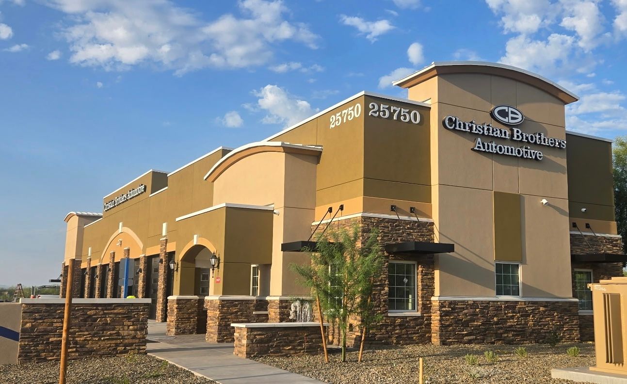 Tan stucco commercial building with blue signage and stone accents under a bright sky