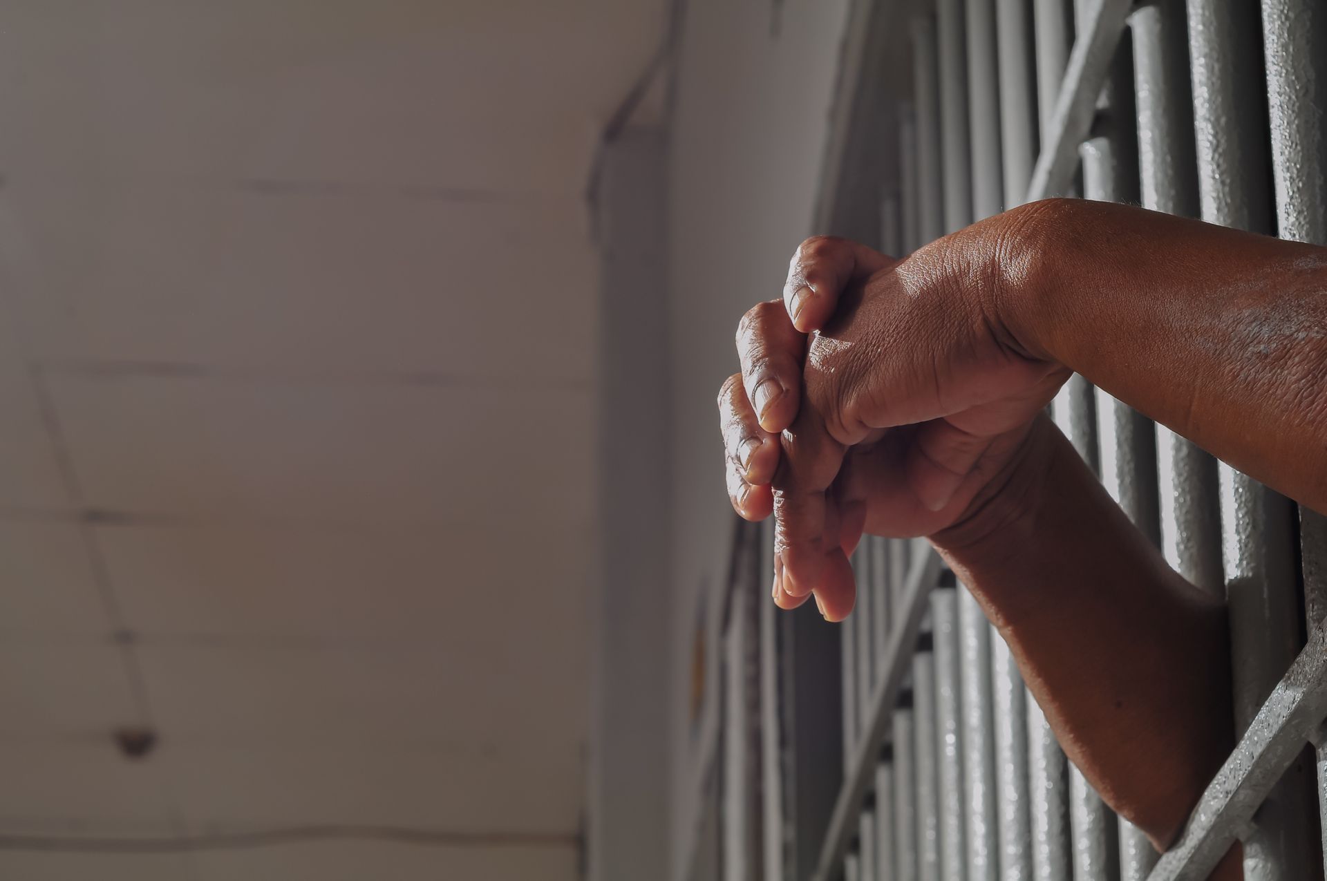 Hands clasped together gripping the bars of a jail cell.