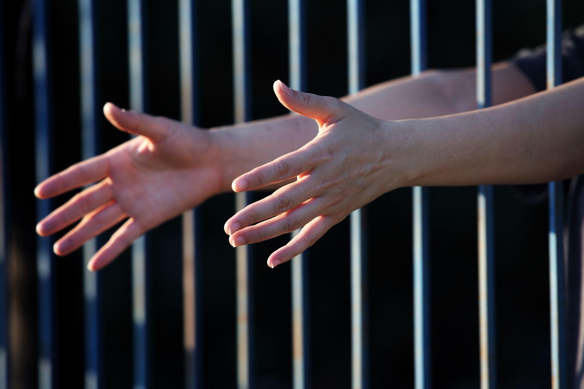 Hands reaching through jail cell bars.