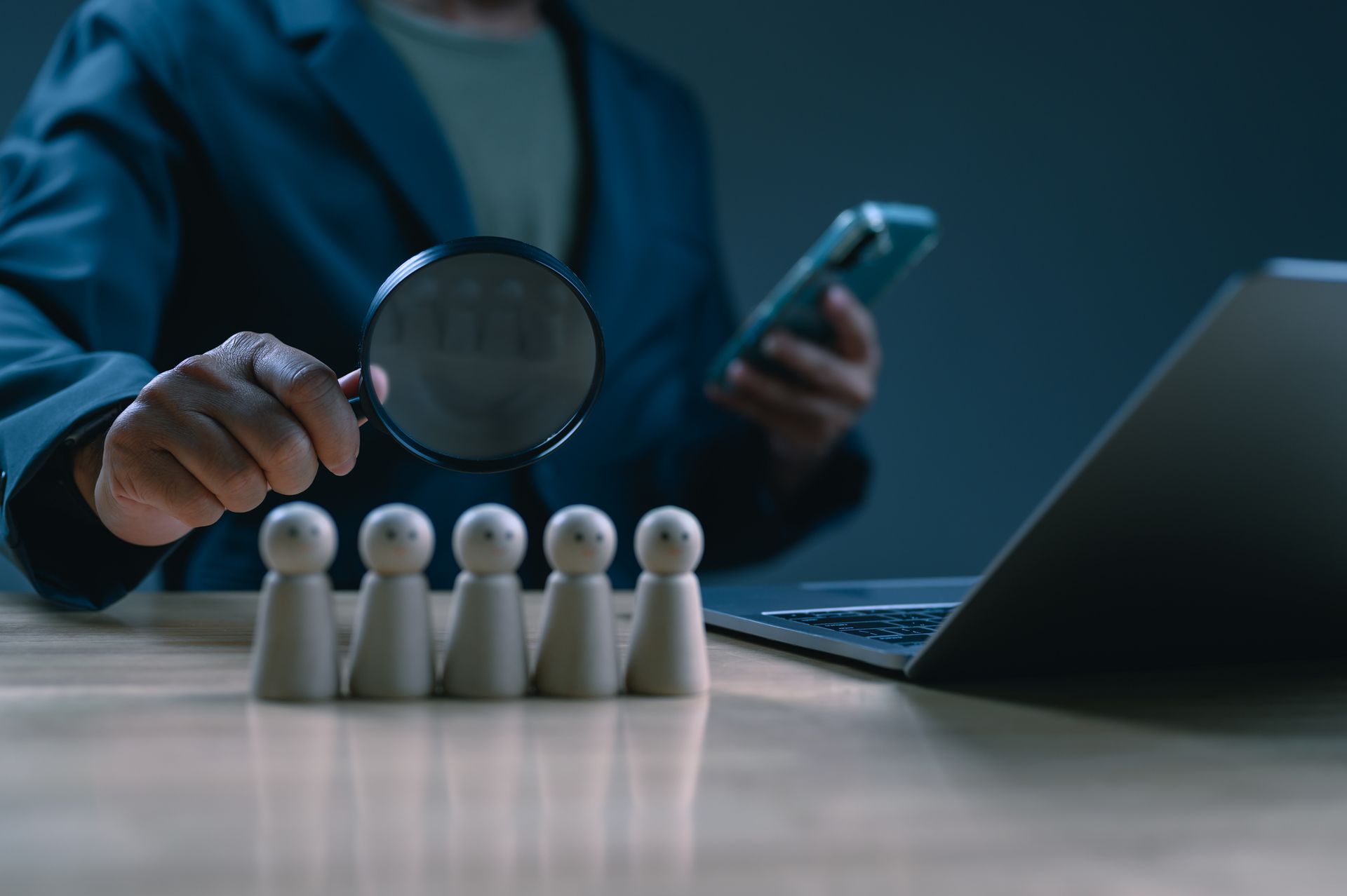 A person holding a magnifying glass, examining wooden figures, showcasing inmate research. A person holding a magnifying glass, examining wooden figures, showcasing inmate research.