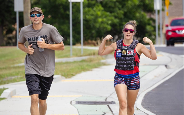 Two runners on a sidewalk, one in gray and one in colorful gear, jogging outdoors on a sunny street.