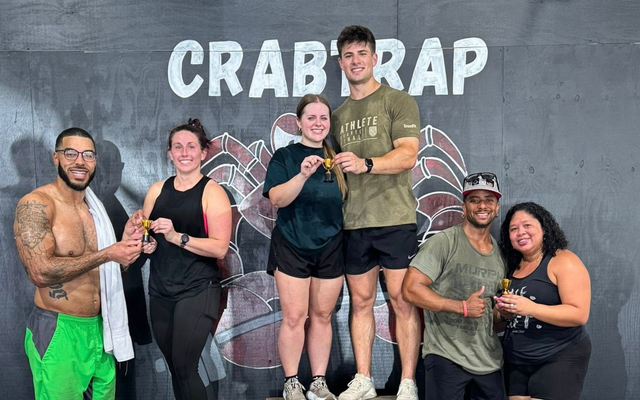 Six people posing with drinks in front of a crab claw backdrop and “CRAB RAB” sign