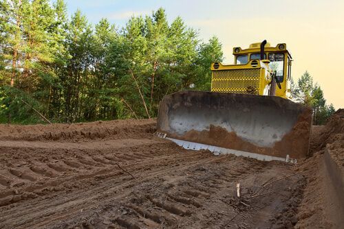 Yellow bulldozer grading dirt in front of a forest.