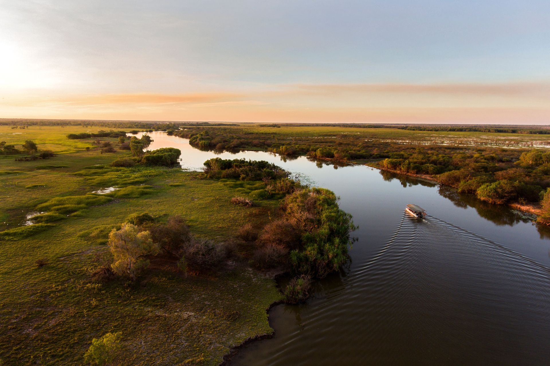 Sunset over winding river through green marshland, with a small boat on the water