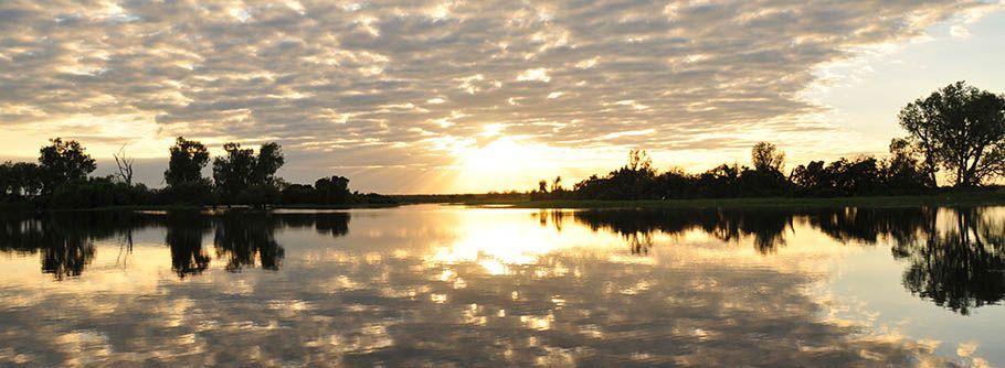 A sunset over a lake with trees and clouds reflected in the water.