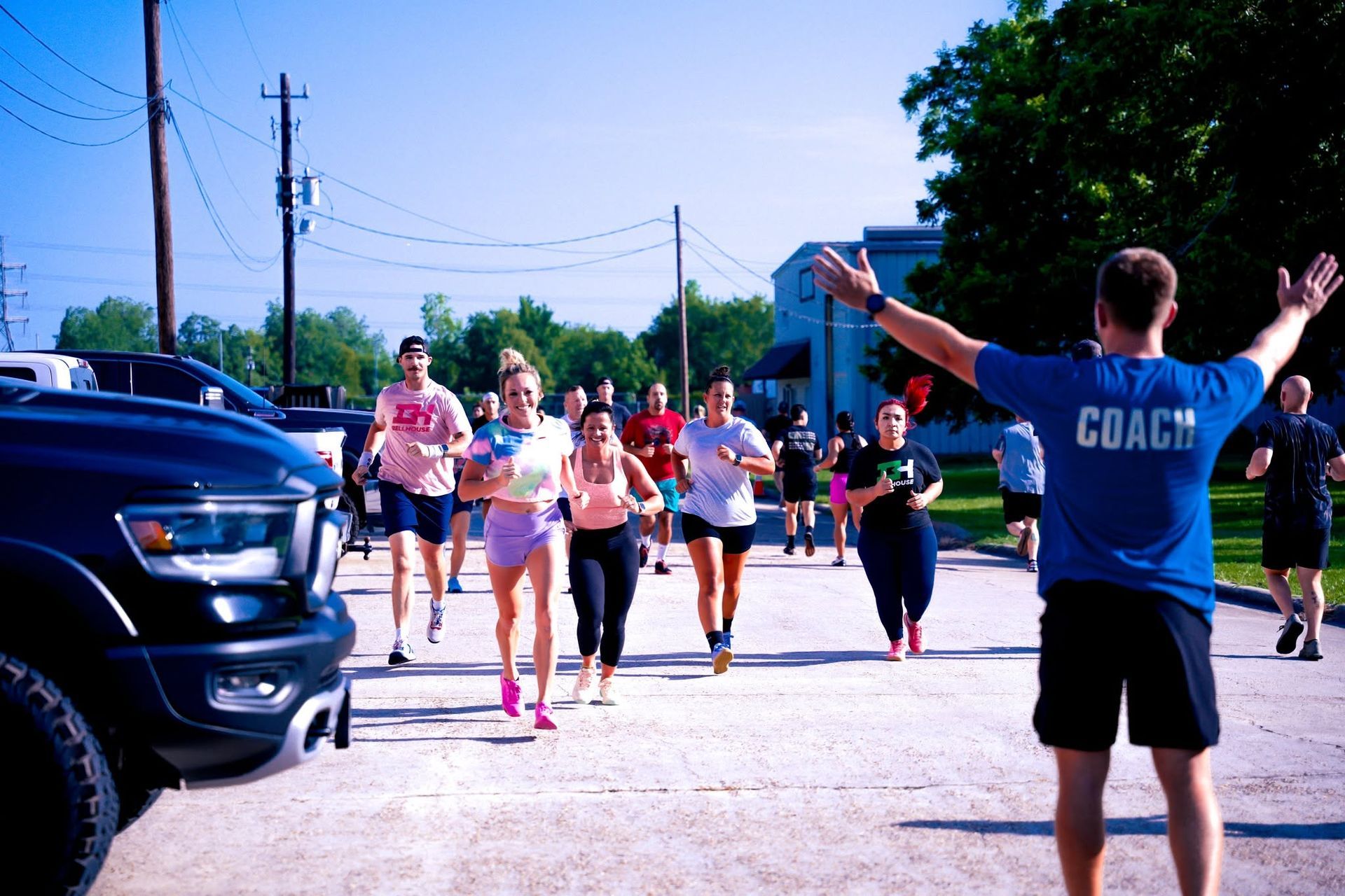Runner approaching finish line on a sunny street, with a coach cheering nearby.