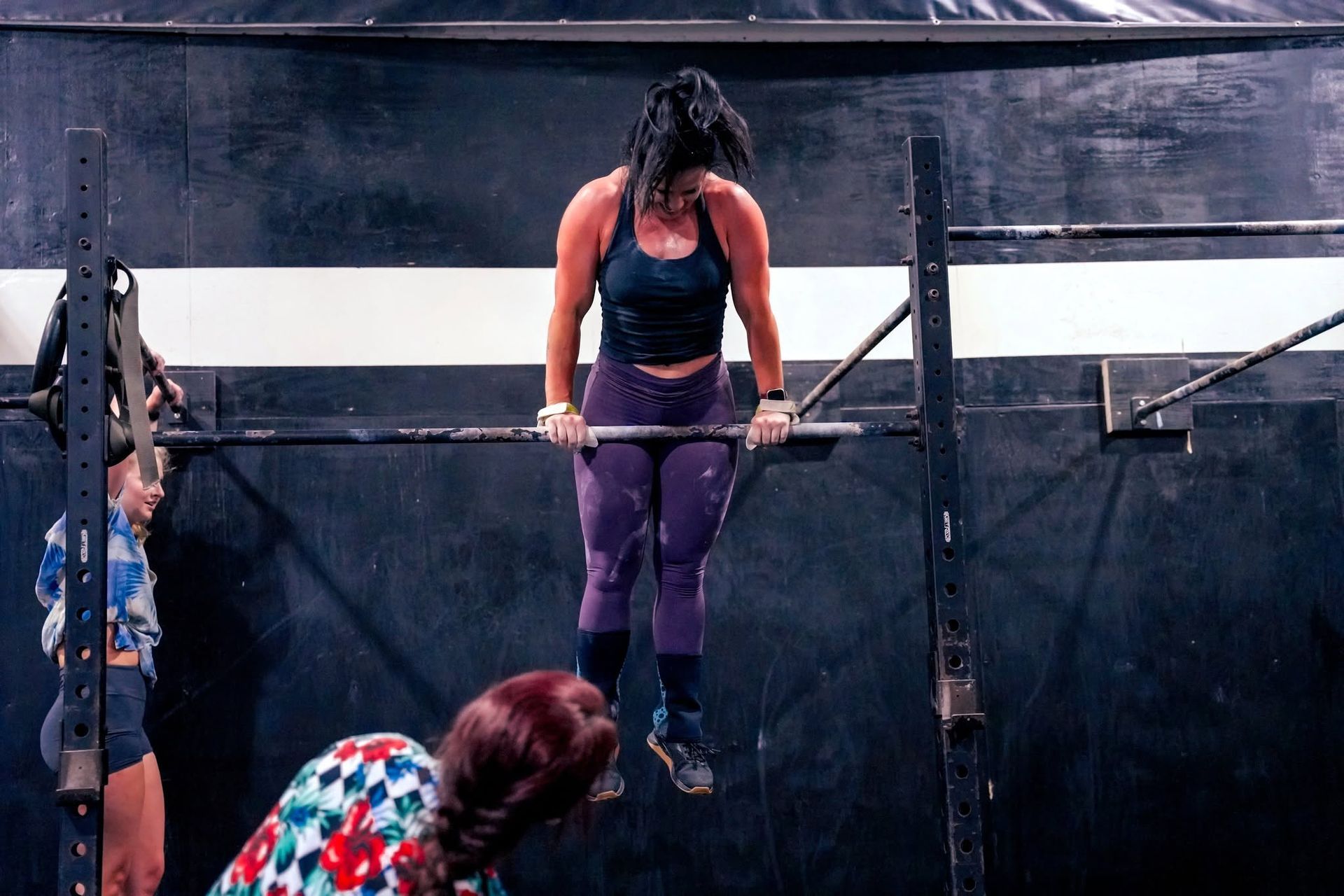 Woman doing a gymnastic hold on parallel bars while another person watches below in an indoor gym in Baytown, TX.