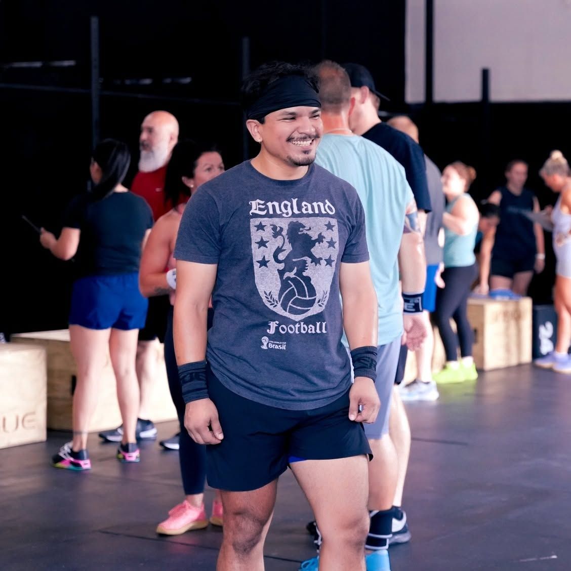 Smiling person in black cap and gray shirt stands in a gym with others in the background