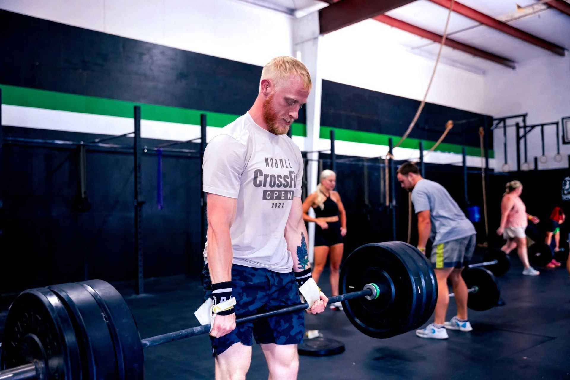 Athlete lifting a heavy barbell in a CrossFit gym in Baytown, TX, with others training in the background.