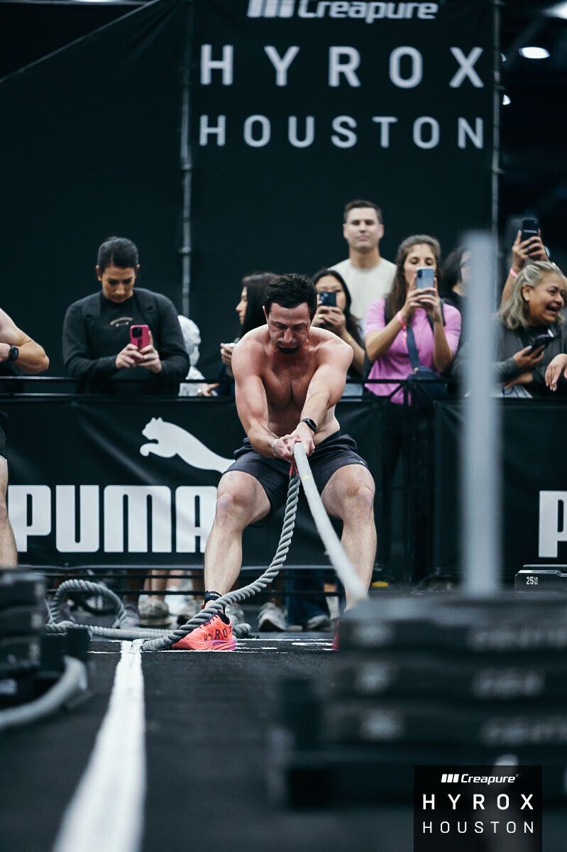 Athlete dragging a rope in a HYROX Houston competition, with spectators and PUMA branding behind him.