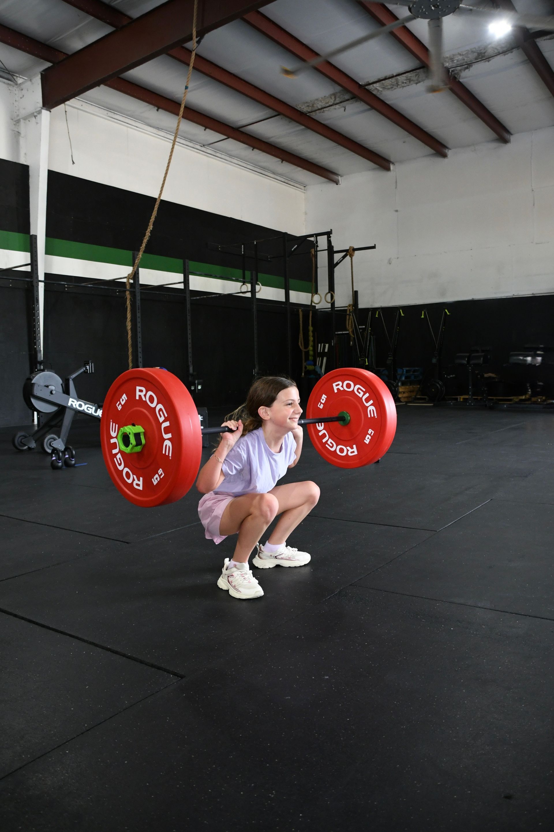 Person squatting with a barbell in a gym in Baytown, TX, holding red weight plates on a black floor.