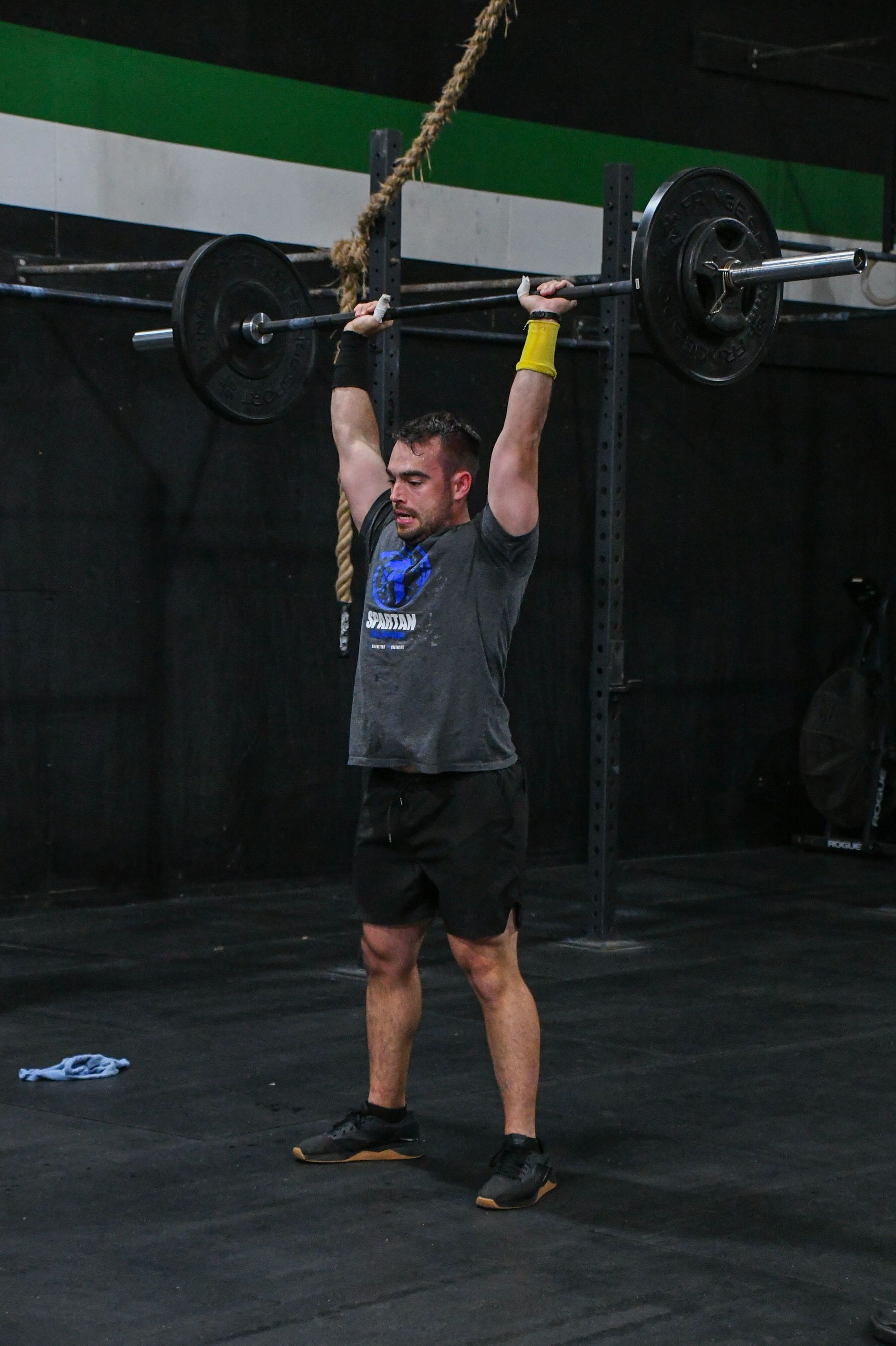 Man lifting a barbell overhead in a gym in Baytown, TX, wearing a gray shirt and black shorts