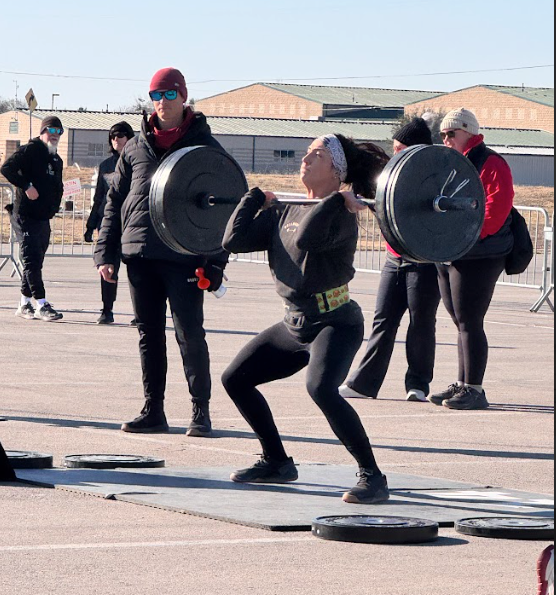 Athletes lifting barbells outdoors in a training area, with weight plates on the ground.