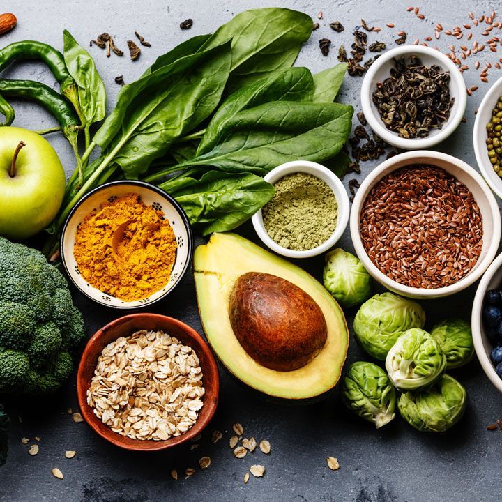 Assorted healthy foods with spinach, avocado, apple, oats, seeds, and spices on a dark surface
