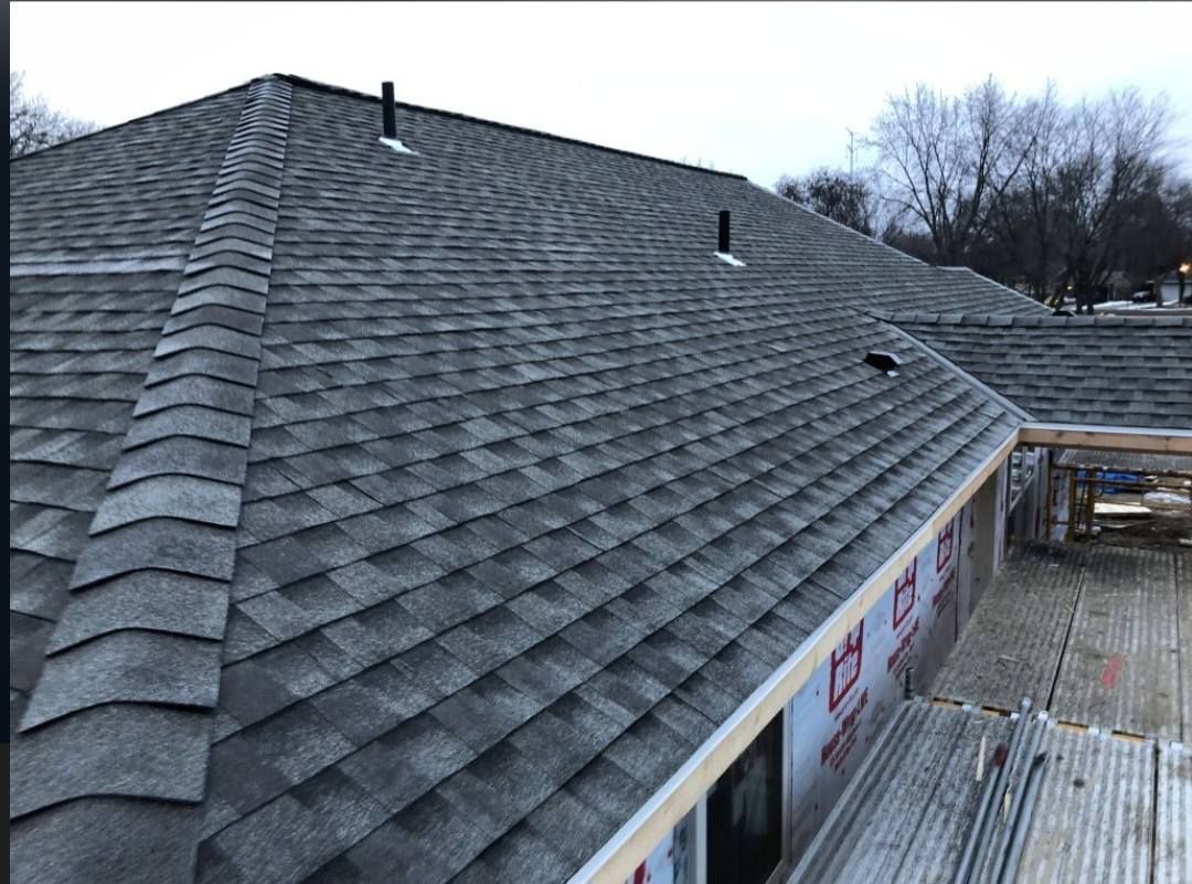 Gray shingled roof with skylights and ventilation pipes on a house under cloudy skies.