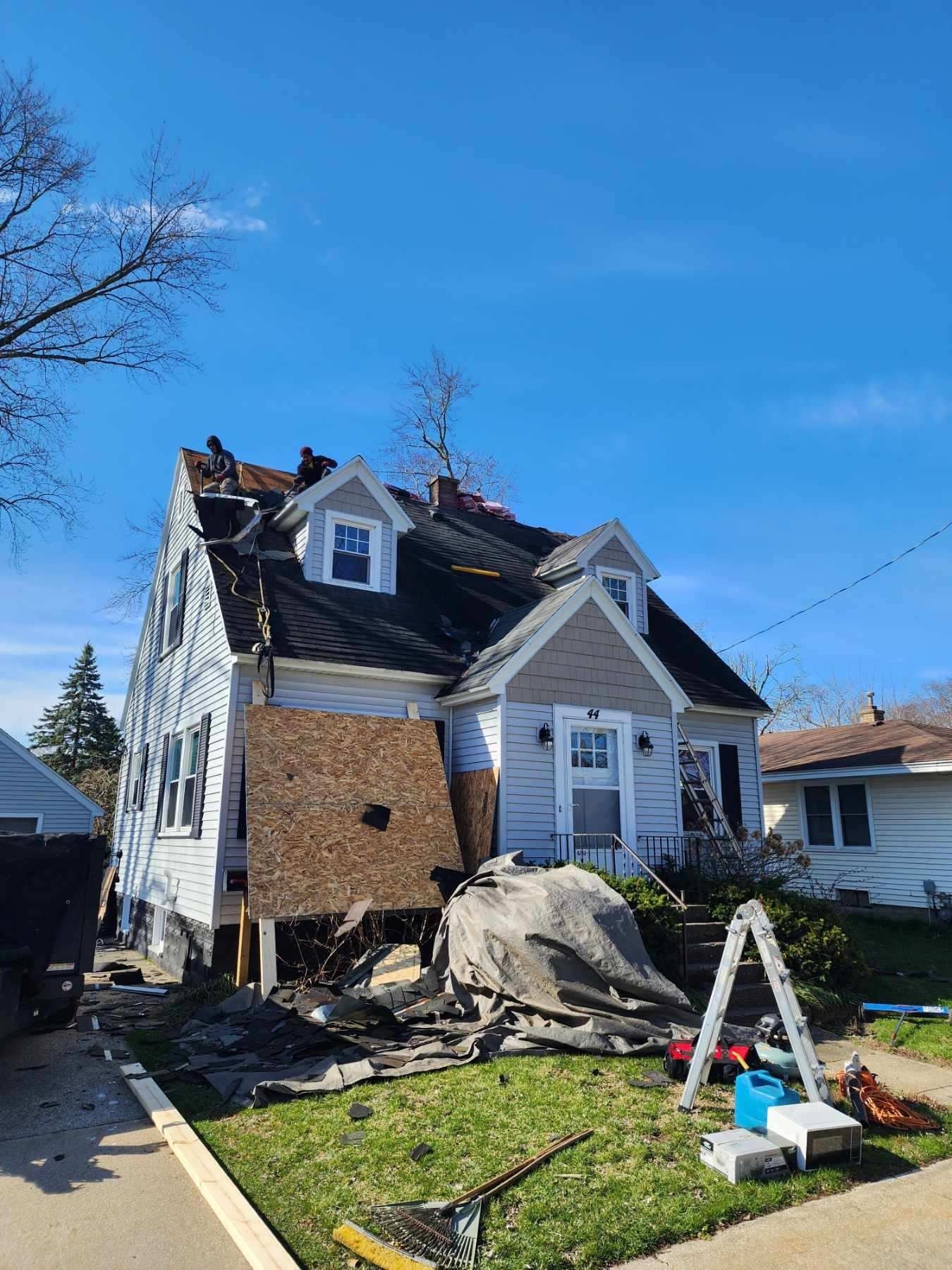 Damaged two-story house with roof torn off, debris in front yard, and blue sky overhead