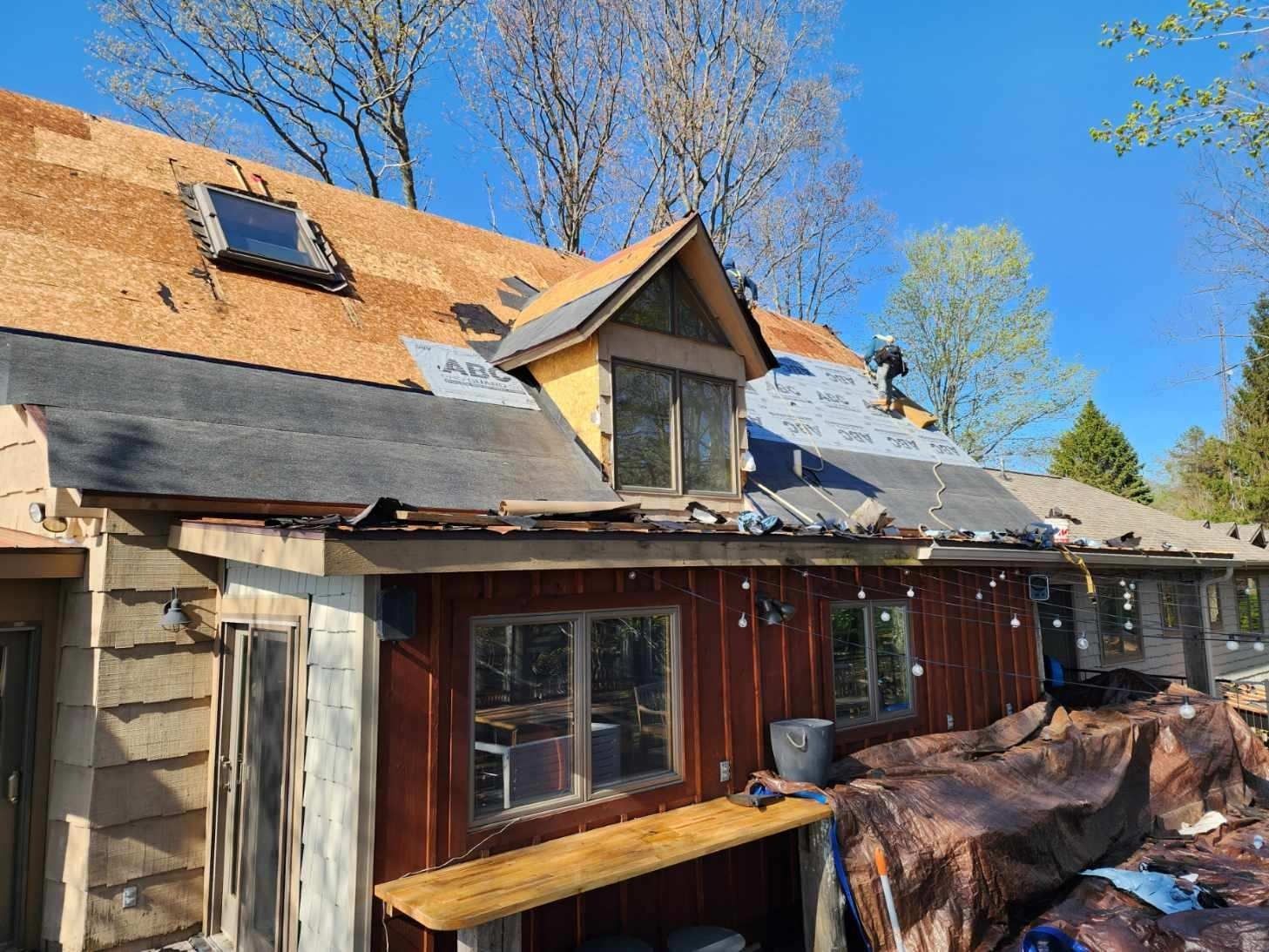 Partially renovated house with exposed roof, windows, and wood siding under a blue sky