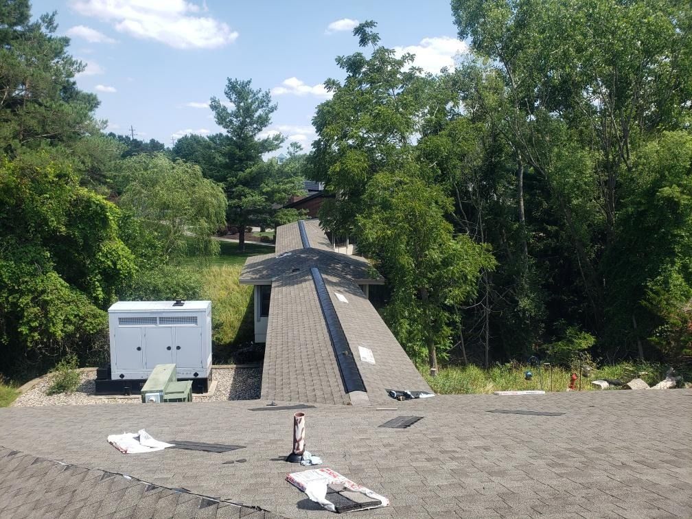Rooftop with a central walkway leading to trees, with a white trailer and materials in the foreground under a blue sky.