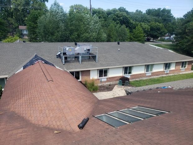 Aerial view of a brick building with a sloped roof, rooftop equipment, and skylights surrounded by trees