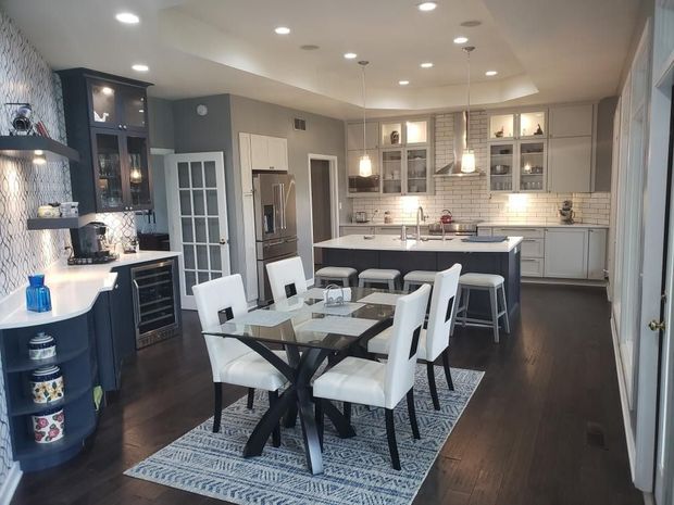 Modern kitchen with dark wood floors, white cabinets, island seating, and a dining table on a patterned rug