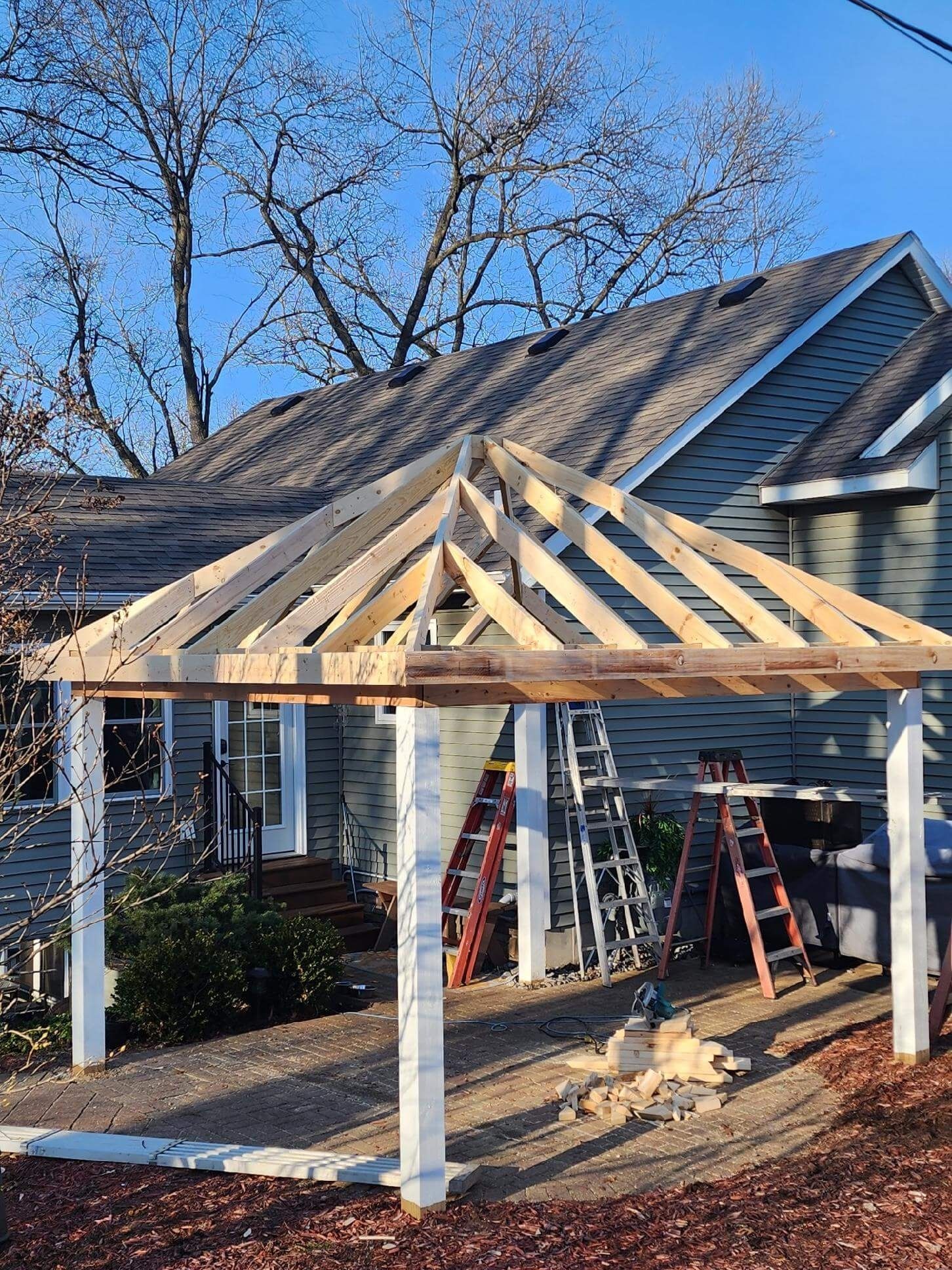 Front porch renovation with new wooden roof framing and support posts on a house