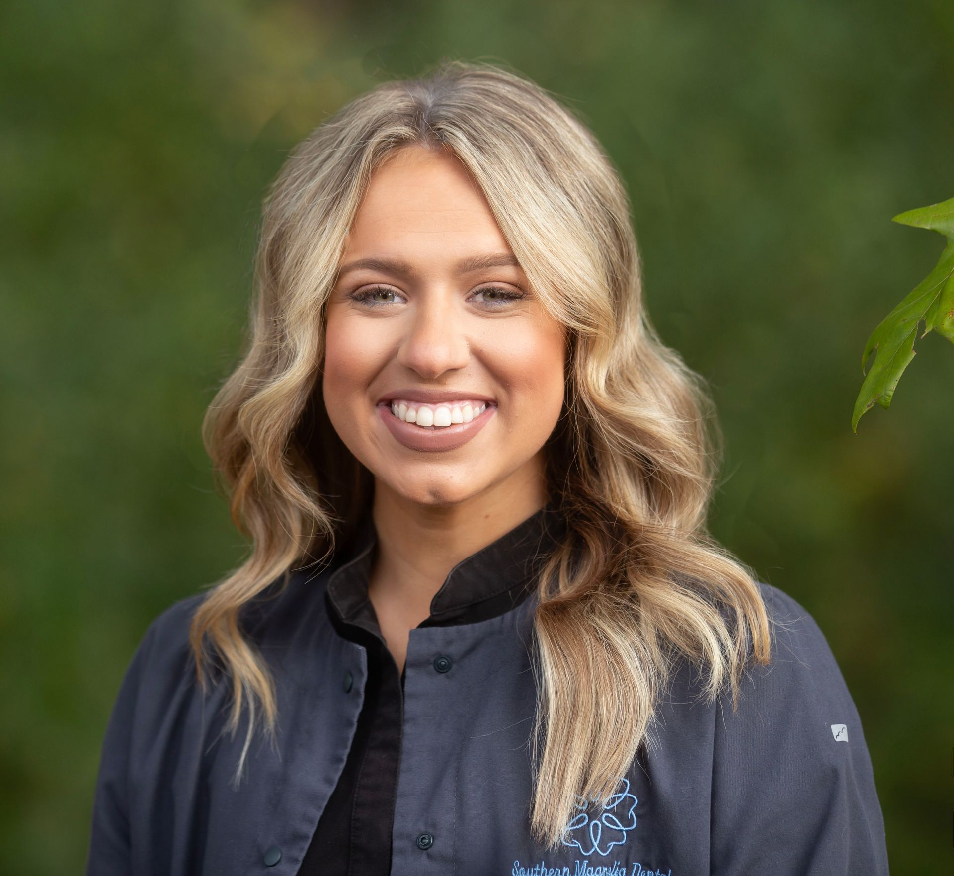Smiling woman in a dark jacket standing outdoors against a blurred green background