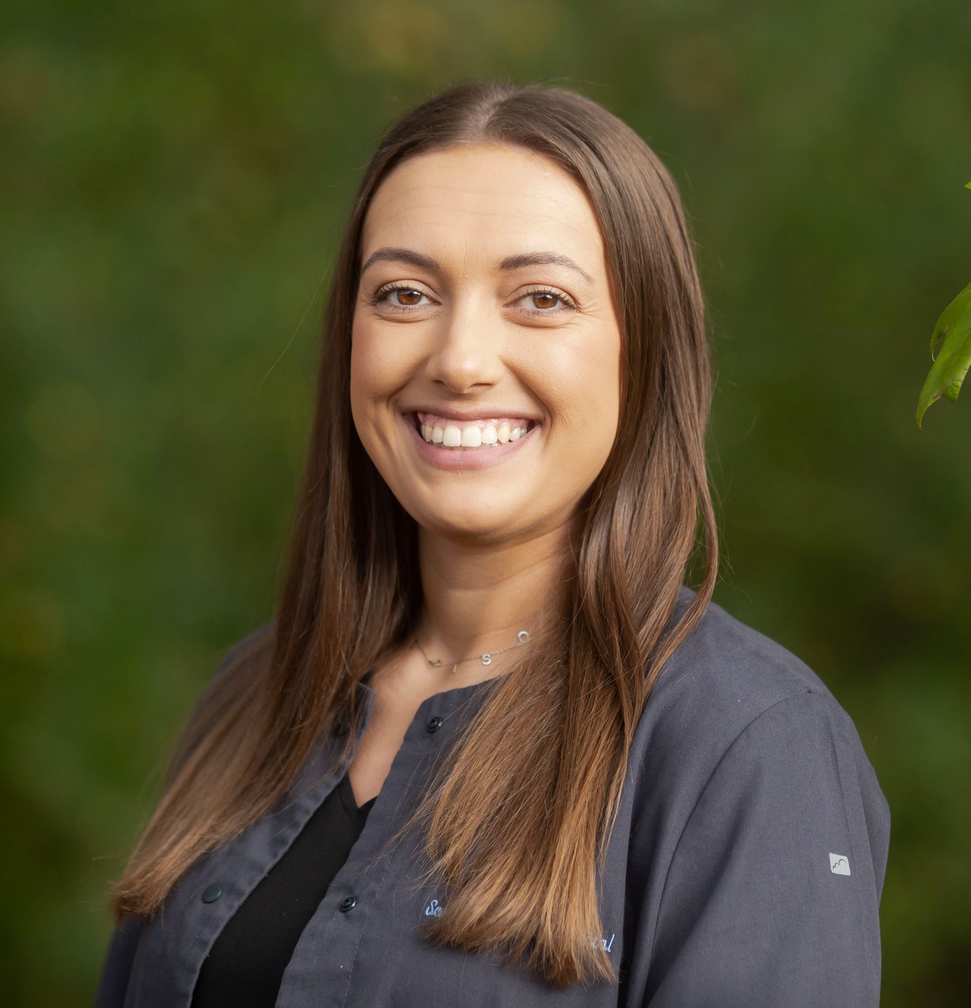 Smiling person in a dark gray shirt against a blurred green outdoor background