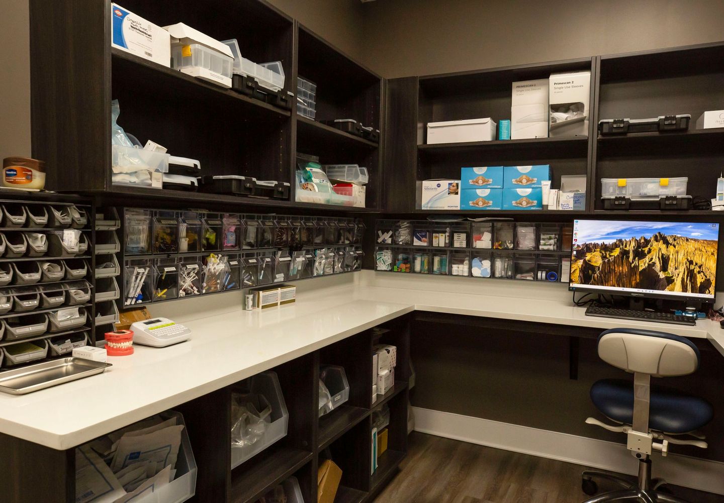 Home office with shelves of storage bins, a desk, and a computer monitor showing a scenic wallpaper.